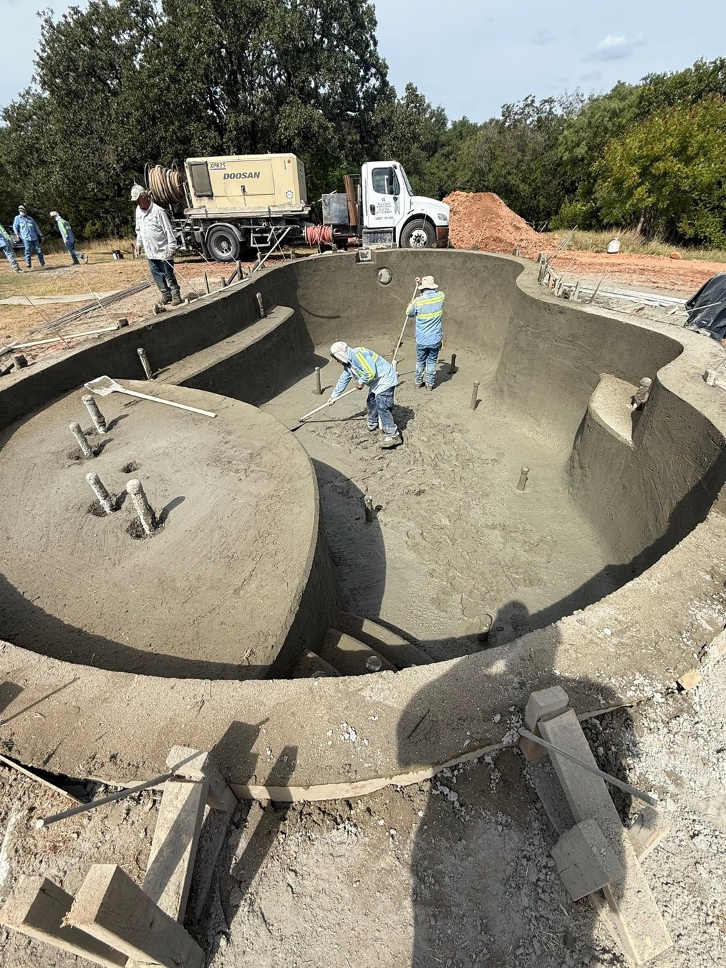 Crew hand-shaping a freshly shot gunite pool shell