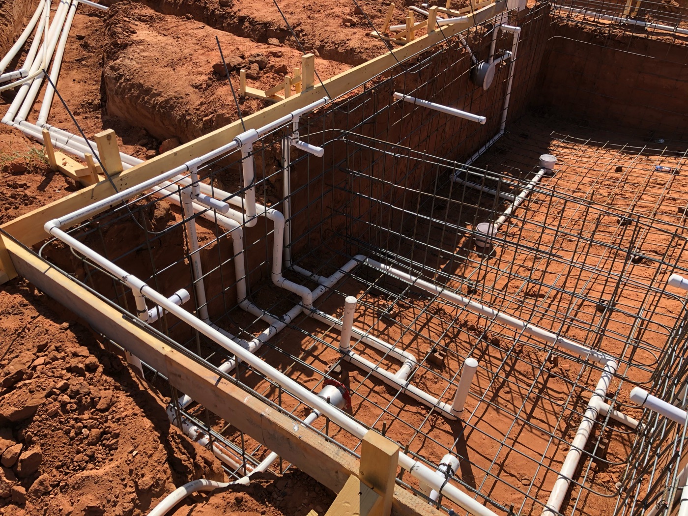 Steel rebar cage and white PVC plumbing installed in a new pool shell