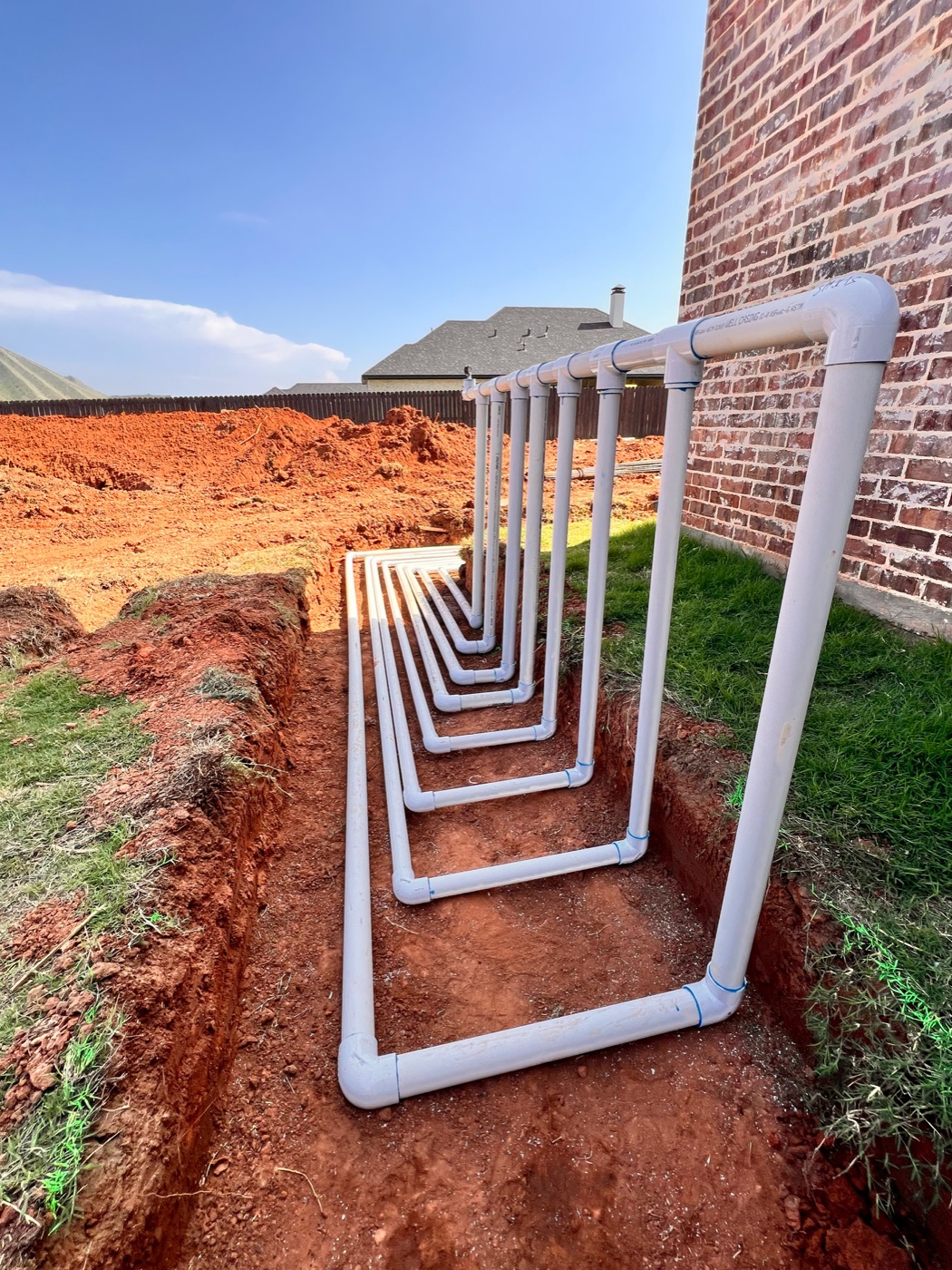 White PVC plumbing runs installed in a trench beside a brick home