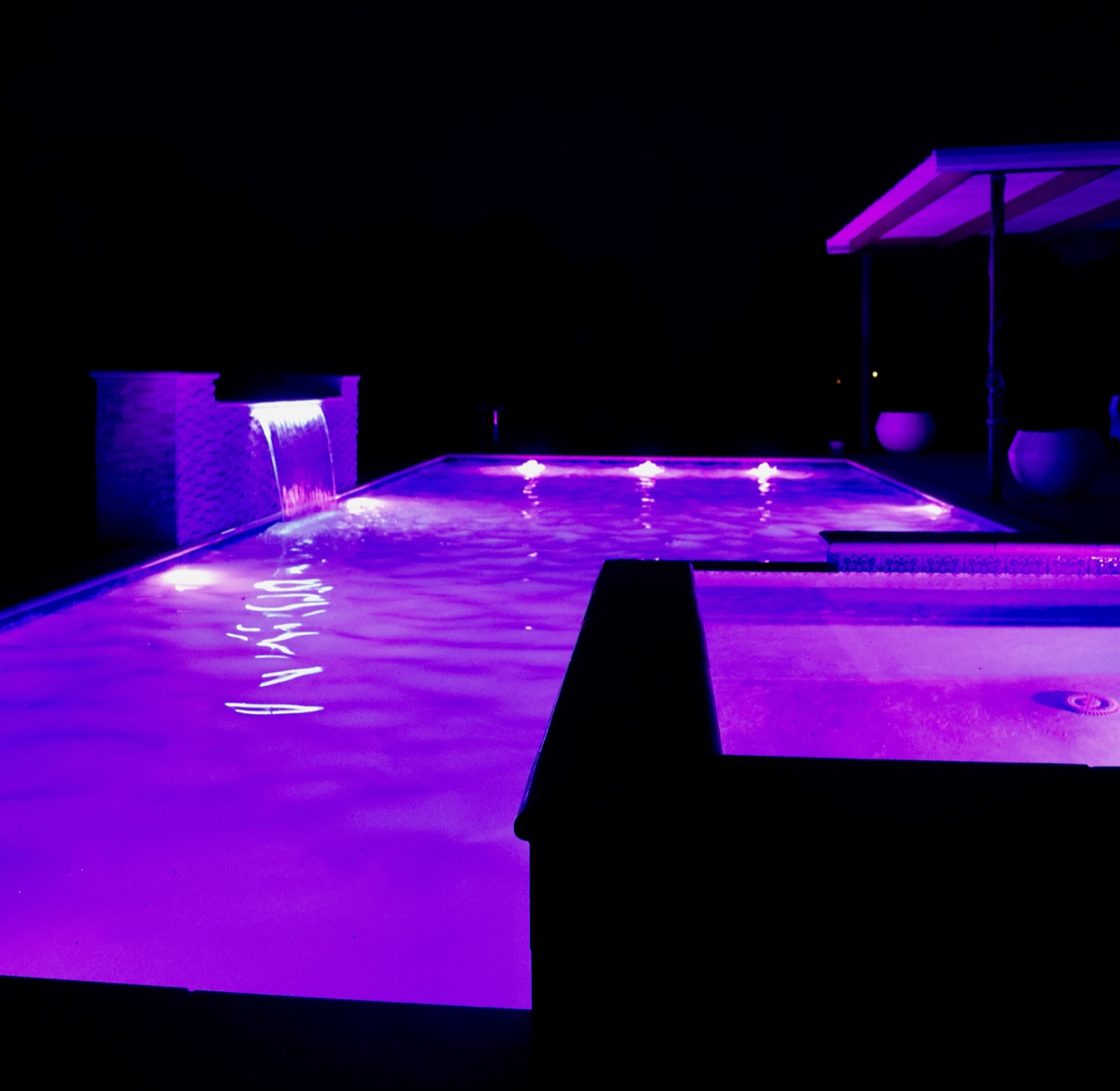 Finished pool lit with color LED lighting and a sheer waterfall at night
