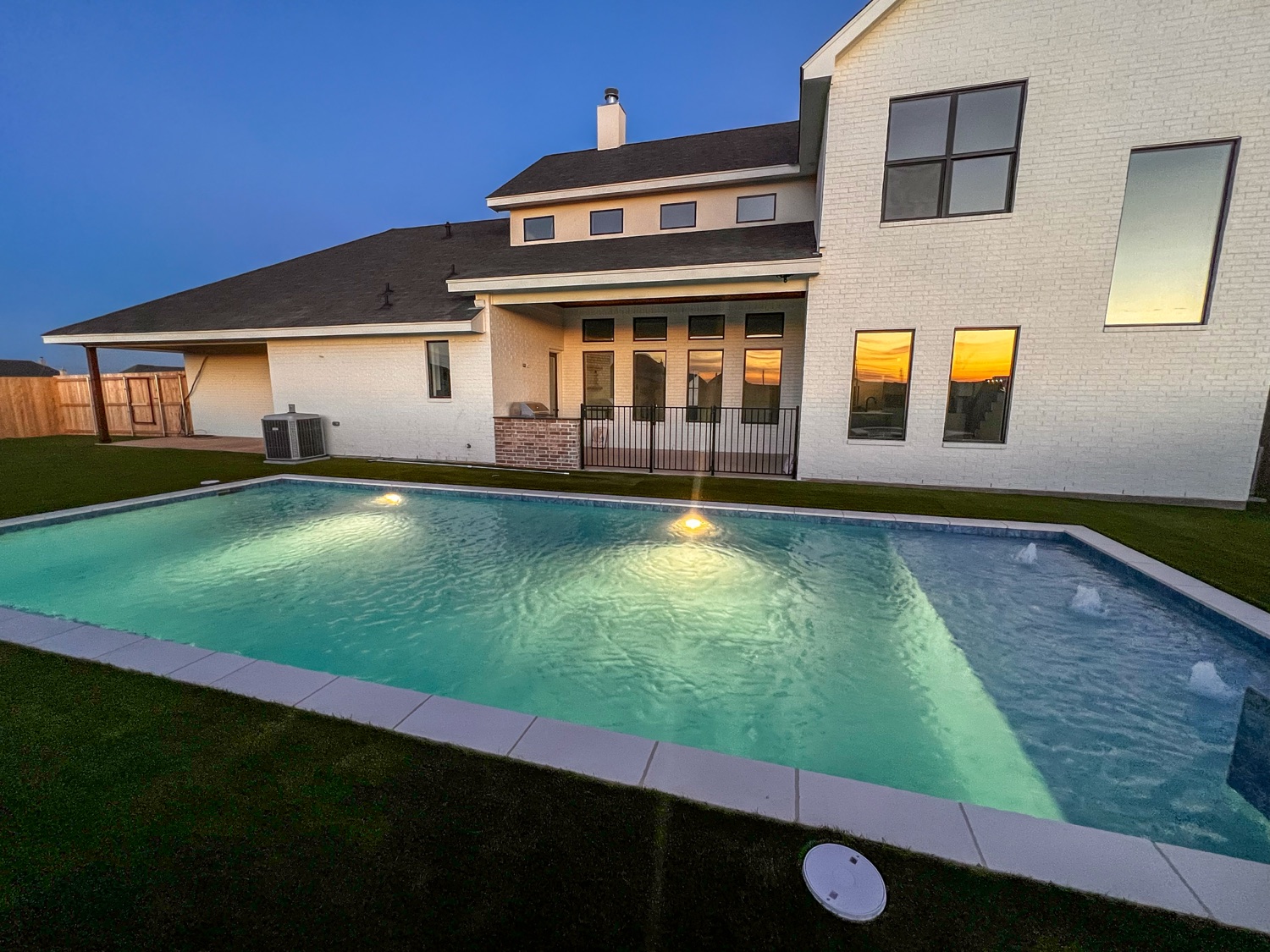 Finished pool glowing at dusk behind a two-story home