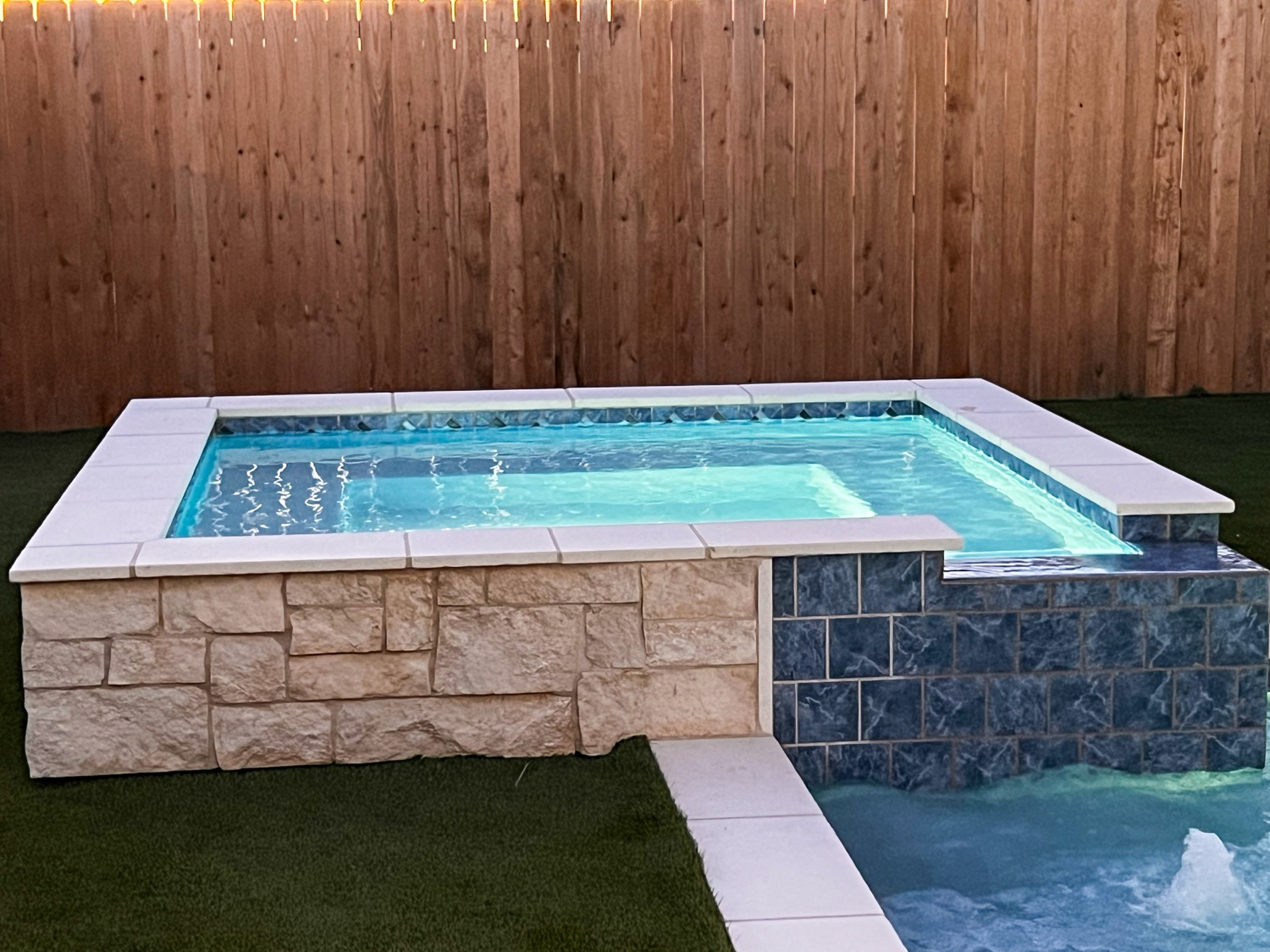 Raised spa with stacked stone and blue porcelain tile glowing at dusk