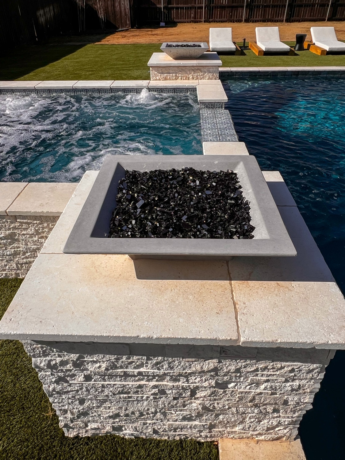 Square glass fire bowl on a stacked-stone pedestal beside a finished pool