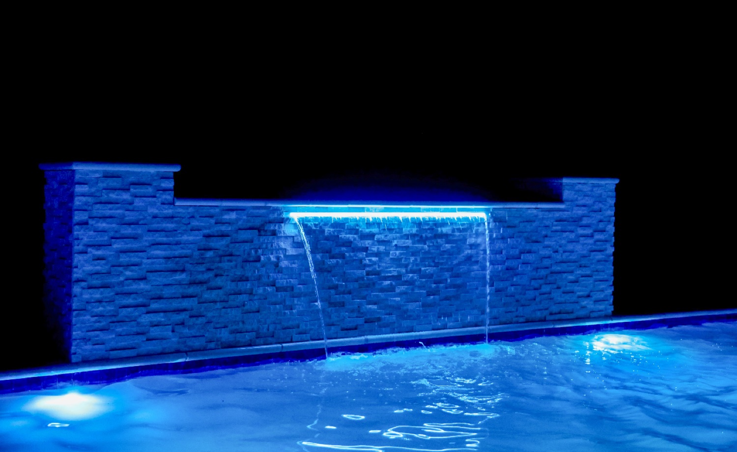 Stacked-stone waterfall wall with a blue LED-lit sheer descent at night