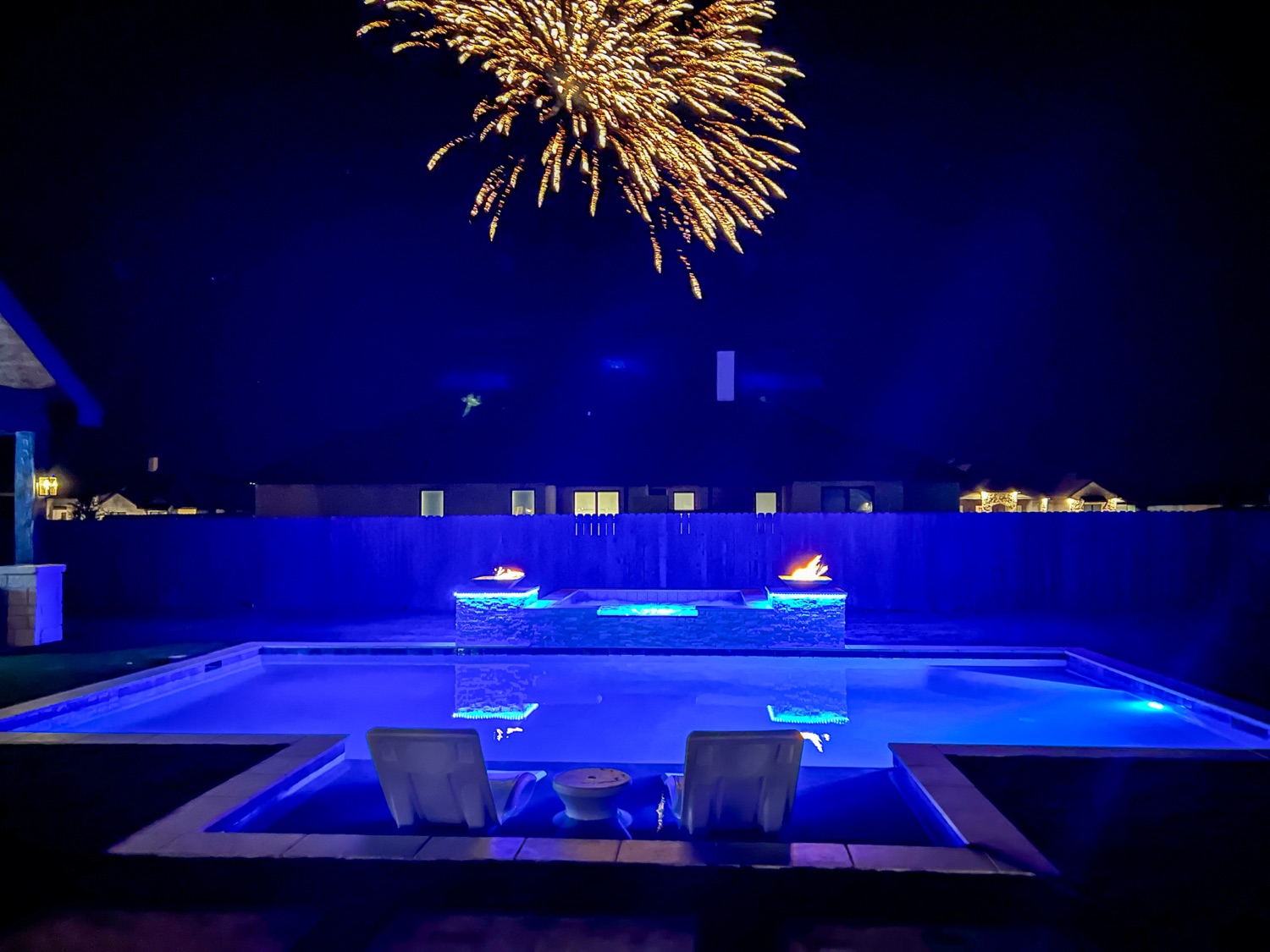 Finished pool at night with lit fire bowls and blue LED lighting